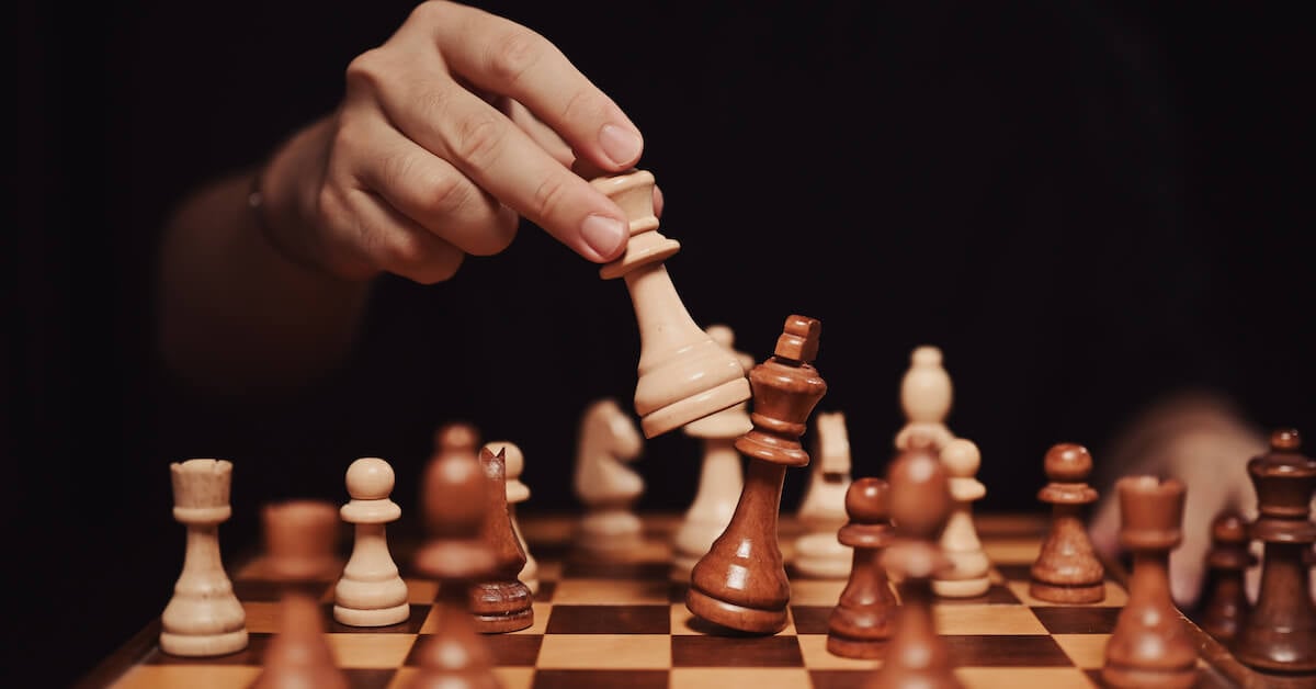 A hand moves a wooden chess piece.