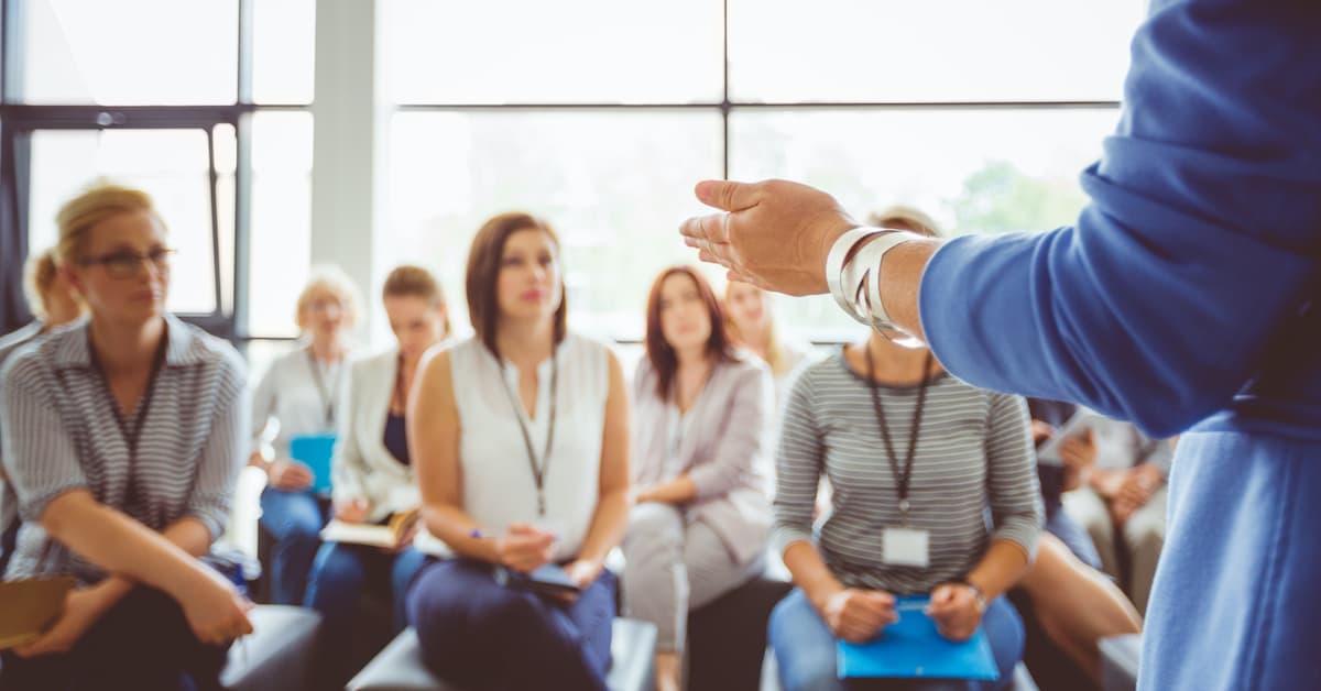 A group of sellers participates in a sales training program, with an instructor at the front of the class