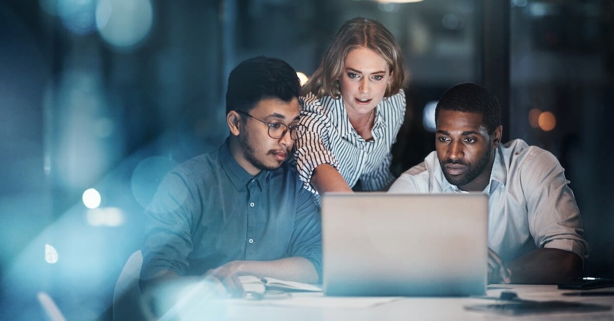 Image of three sales professionals gathered around a laptop, with one explaining an AI tool